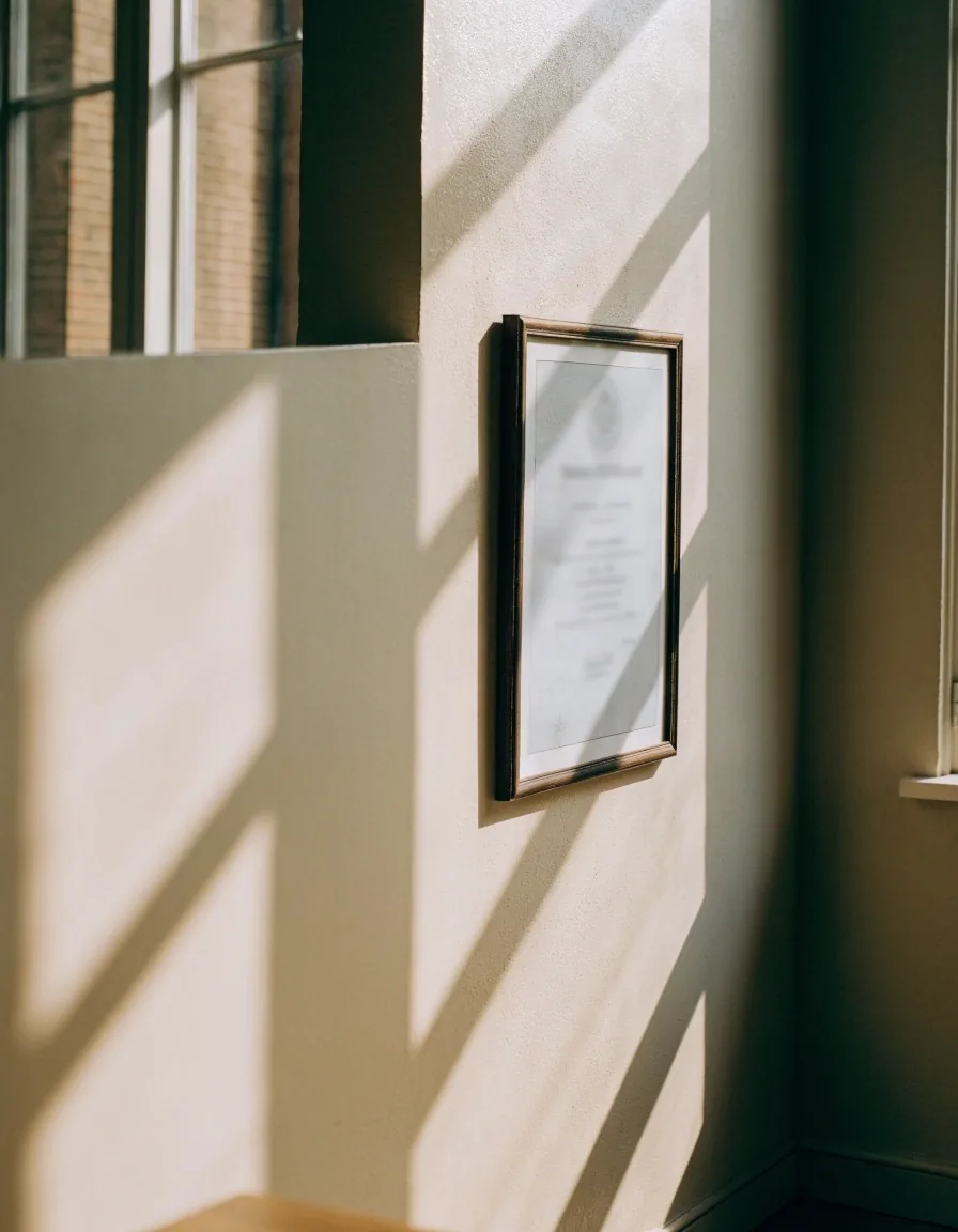A framed accreditation certificate hanging on a plain school office wall, its printed face out of focus
