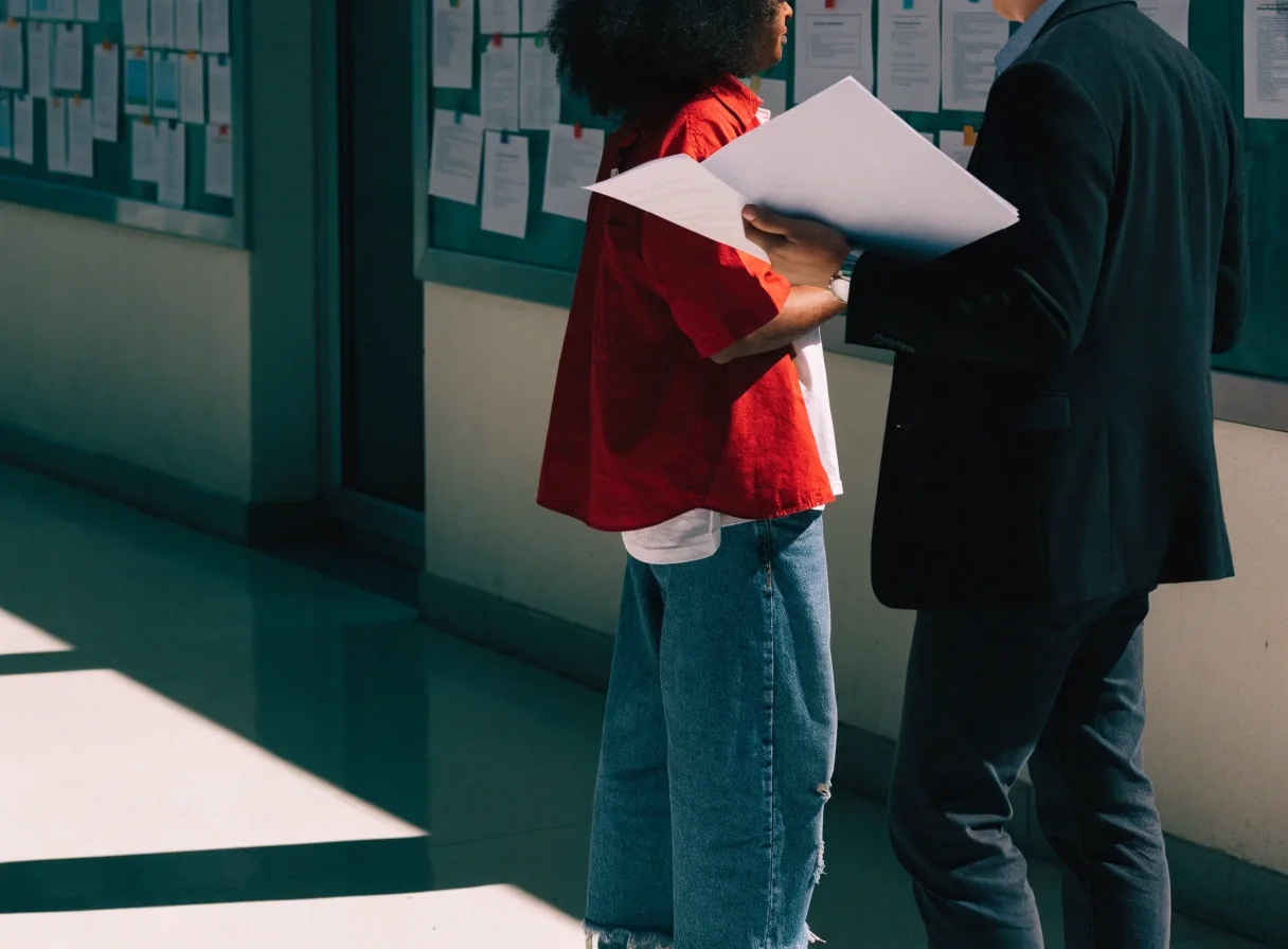 Two adults in conversation at the corridor noticeboard of a London English language school